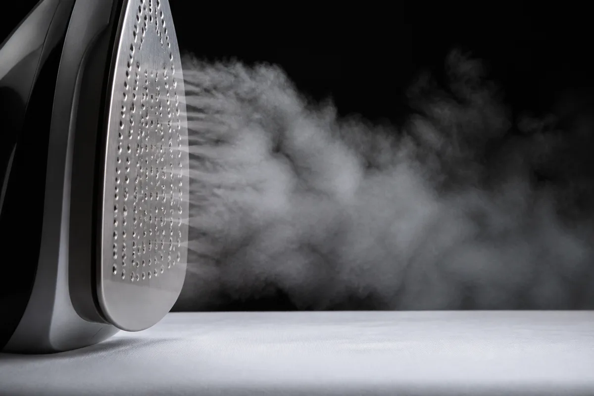 Gros plan sur une semelle de fer vapeur libérant un panache de vapeur au-dessus d&rsquo;un drap blanc tendu