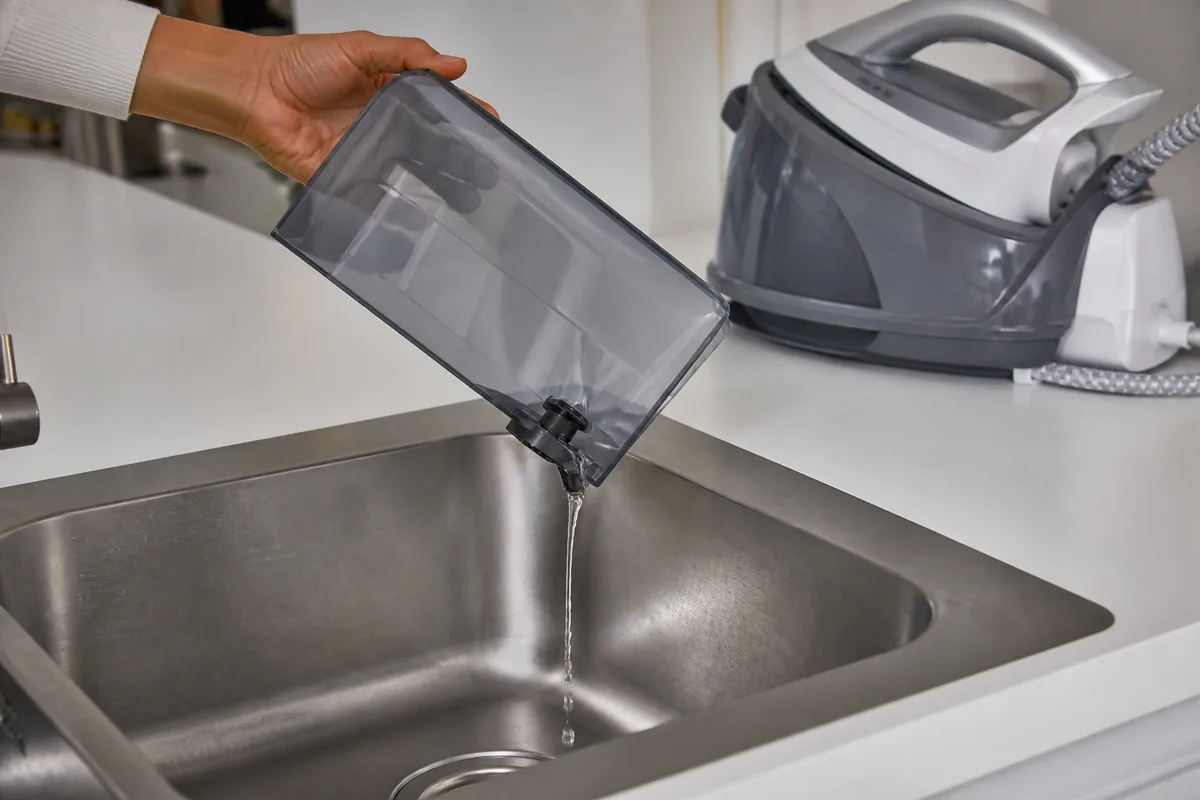 Réservoir amovible transparent retiré d&rsquo;une centrale vapeur et vidé au-dessus d&rsquo;un évier en inox